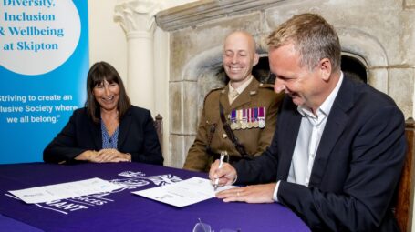 two men and one woman sitting at a desk, one of the men is signing a document