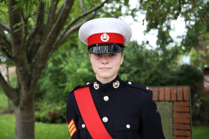 Cadet Sergeant Gemma Carr in uniform standing smiling in front of some trees