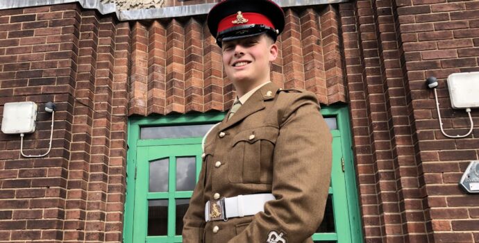 Cadet Matthew McGowan dressed in army uniform standing in front of a building looking down and smiling into the camera