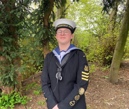 Sea cadet Talitha Ridley wearing her uniform stands in front of some greenery