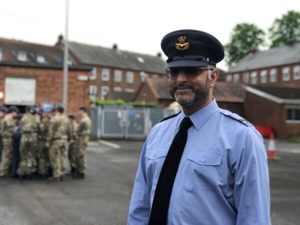 Cadet force adult volunteer, Zia Mir, standing in his uniform with a group of air cadets in the background